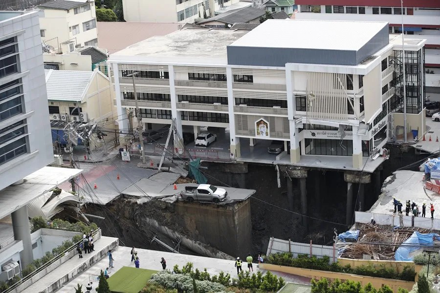 Funcionarios tailandeses inspeccionan un gran socavón donde una camioneta quedó atrapada tras un derrumbe en Bangkok